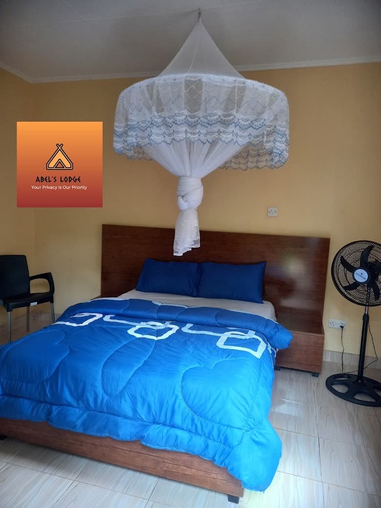 Guest room with a double bed in blue linen, a white mosquito net, a wooden headboard and a standing fan